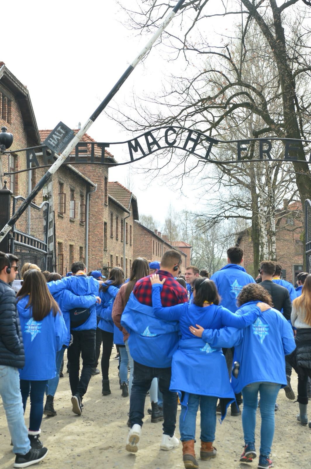 March of the Living students in blue jackets enter Auschwitz beneath the gate