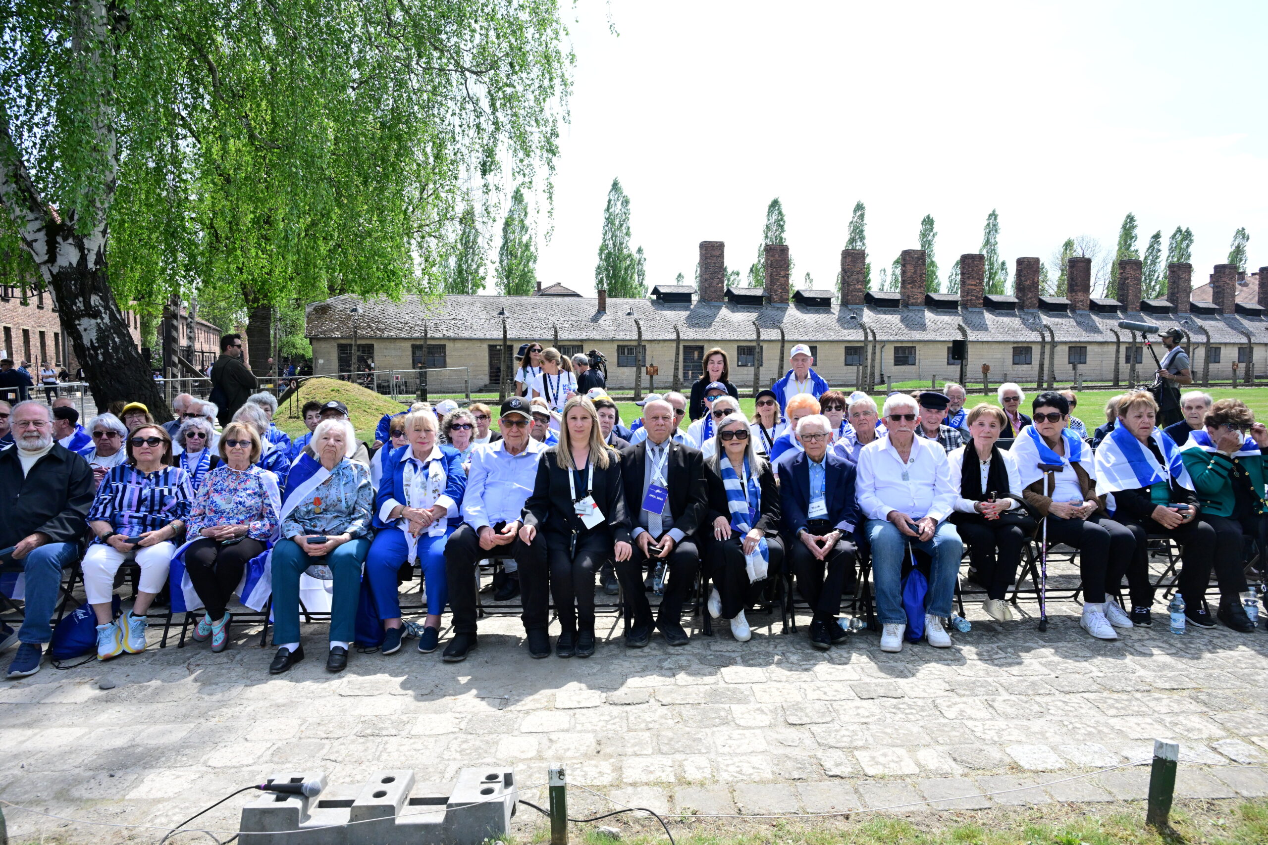 Marchers and survivors in blue jackets seated at the 2025 ceremony at Auschwitz-Birkenau