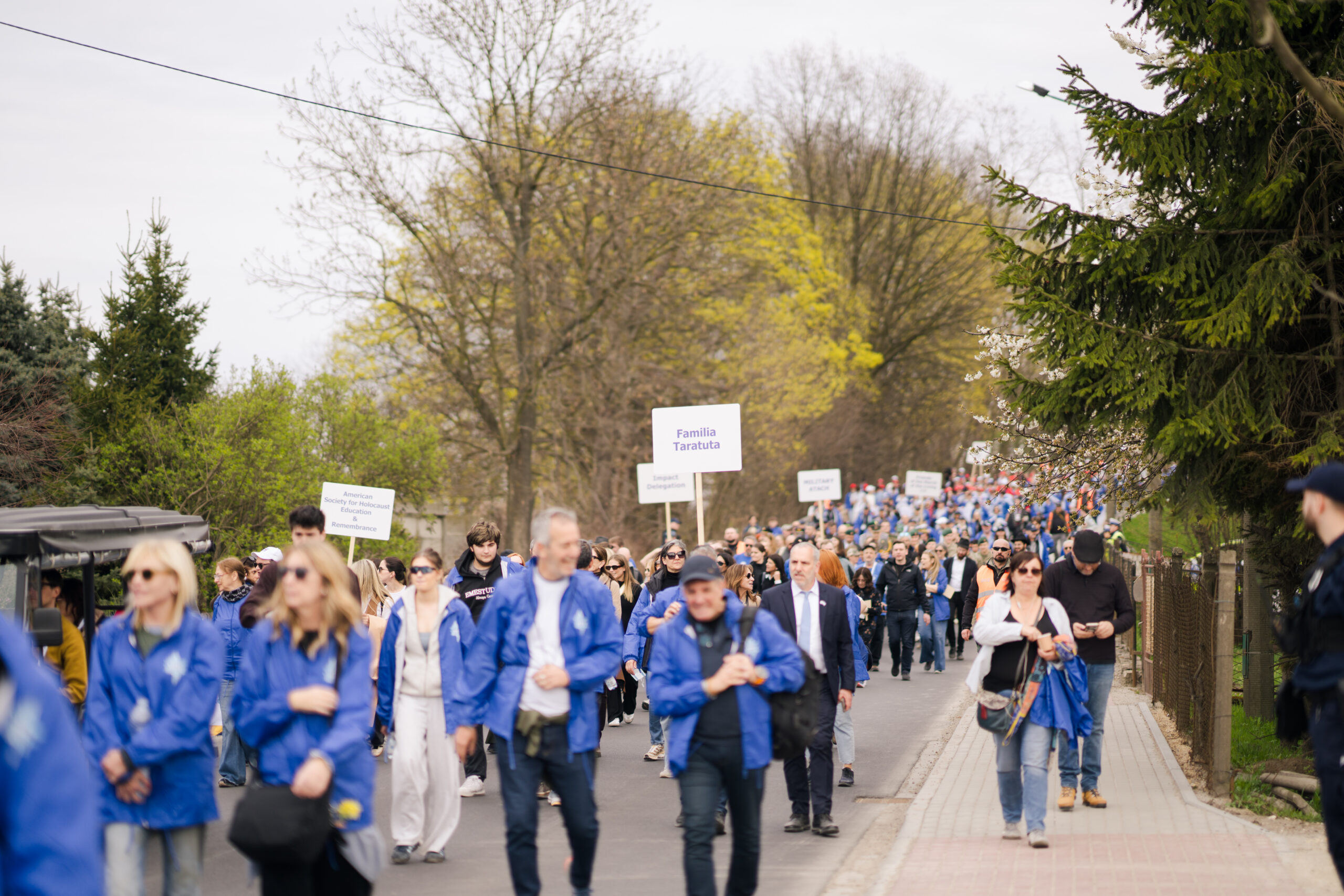 Marchers in blue March of the Living jackets walking along a tree-lined path in Poland, 2026
