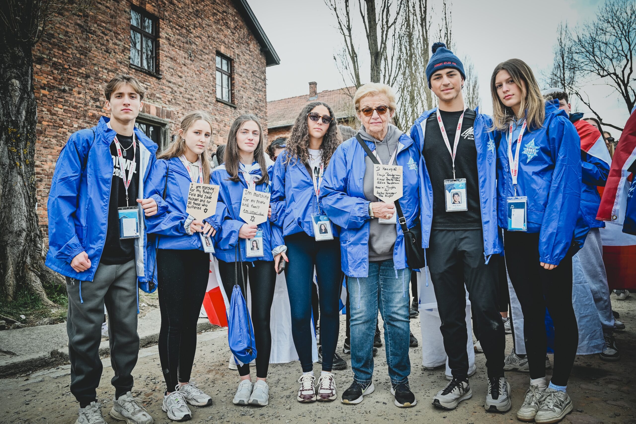 A Holocaust survivor stands with students holding handwritten memorial signs at Auschwitz