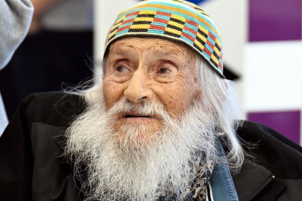 Older man with a long white beard wearing a colorful knit cap and dark jacket, looking off to the left.