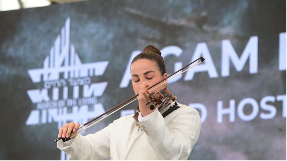 Agam Berger plays a violin in front of the March of the Living logo at the 2025 March of the Living